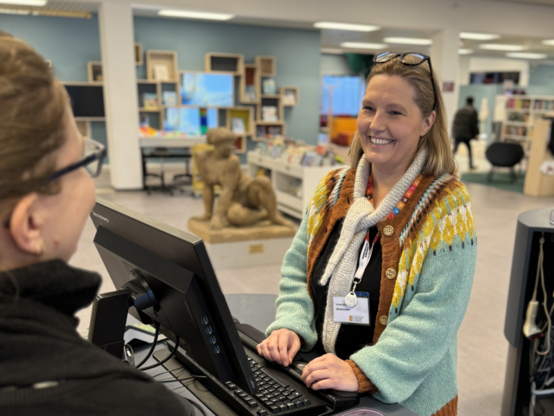 Foto af personalet på biblioteket der smiler mens de betjener en biblioteksbruger