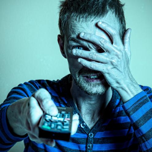 En mand ser fjernsyn, men holder sig for øjnene.